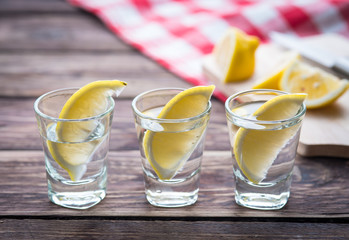 Vodka with lemon in shot glass on wooden background