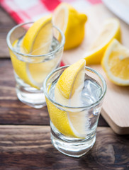 Vodka with lemon in shot glass on wooden background