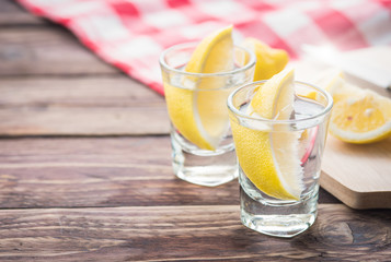 Vodka with lemon in shot glass on wooden background