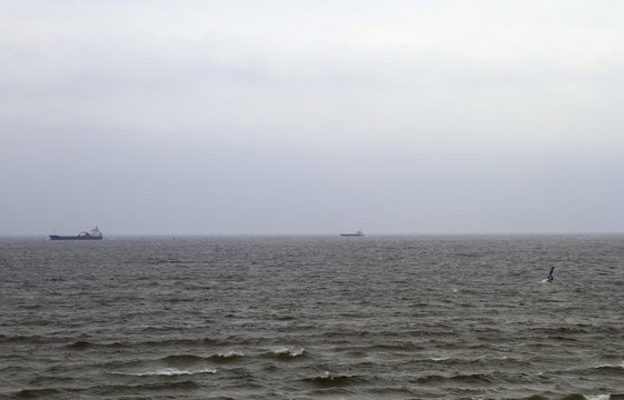 grey sky with two ships, kite surfer and waves in the sea