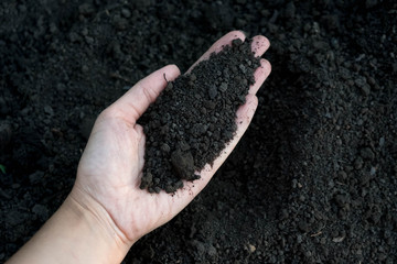 Female hand holding a handful of rich fertile soil that has been newly dug over or tilled in a concept of conservation of nature and agriculture. Blurred motion the soil falling to the ground.