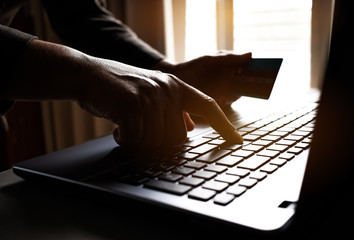 Black hands of anonymous hackers holding credit card and using, typing code on keyboard of laptop...