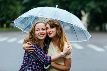 Two joyful hipster girl sheltering from rain beneath umbrella - they loves a rain and rejoices....