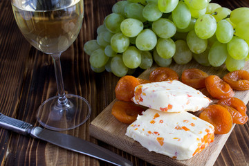 Soft cheese with dried apricots, glass of wine and fruit on the wooden background