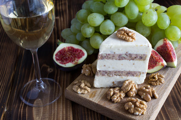 Soft cheese with nuts, glass of wine and fruit on the wooden background