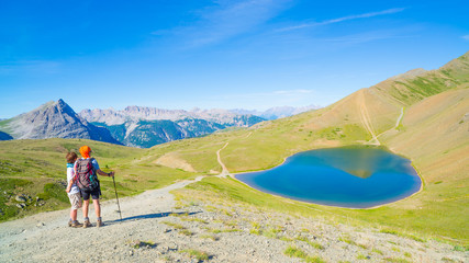 Couple of hiker on the mountain top looking at blue lake and mountain peaks. Summer adventures on the Alps. Wide angle view from above.