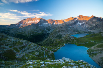 High altitude alpine lake, dams and water basins in idyllic land with majestic rocky mountain peaks glowing at sunset. Road leading to mountain pass on the Alps.