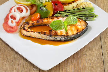 Salmon grill on teriyaki sauce and vegetable grill in white dish on the wooden table