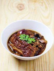 Closeup stewed pork leg in gravy soup and herb on wood table