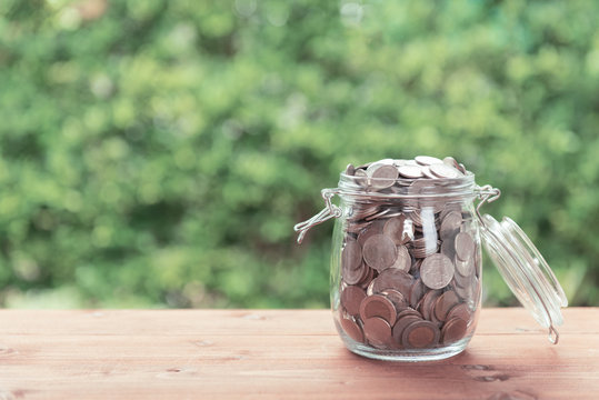 Money coins in glass jar on old  wooden table with green nature background