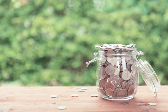 Money coins in glass jar on old  wooden table with green nature background,saving money concept