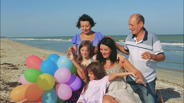 Happy family. Grandmother, grandfather, Loving mother and youngest daughter and an seventeen-year-old daughter with Down syndrome on the beach With balloons.  Positive human emotions, feelings.