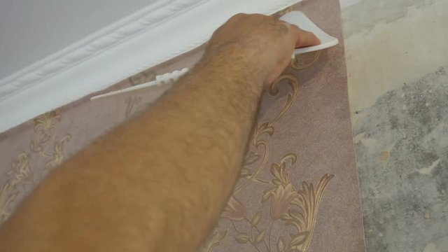 the process of gluing Wallpaper on the wall,the hand of the worker to smooth the Wallpaper with a spatula clamping.