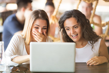 Two young women having fun and laughing while looking at laptop