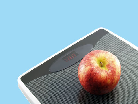 apple on grey digital weight scale isolated on blue, weight control by eating fruit