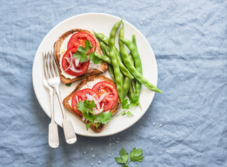Tomatoes, cream cheese toast and green beans on a blue background, top view. Delicious healthy breakfast or snack