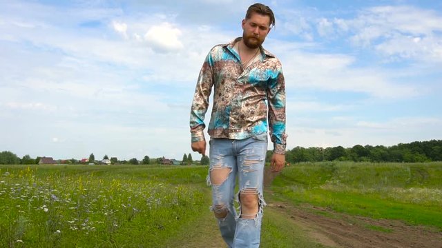 A man with a beard in ripped jeans walking along the field on a summer day