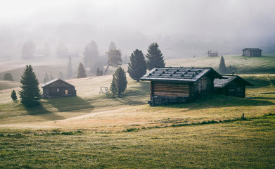 Fototapeta premium Alpe di Siusi (Seisser Alm) meadows and traditional old mountain chalets on foggy sunrise. Trentino Alto Adidge, Italy.
