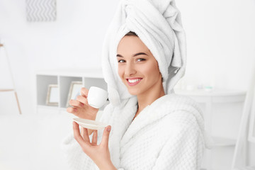 Beautiful young woman after shower in bathrobe with cup of coffee indoors