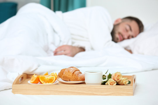 Tray With Breakfast In Hotel Room And Sleeping Man On Background