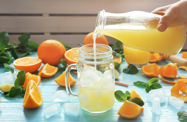 Young woman pouring orange juice from bottle into glass jar on table