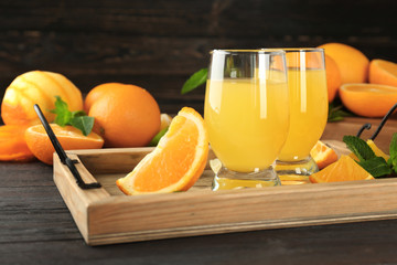 Glasses with delicious orange juice and ingredients on wooden tray