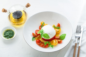 Italian appetizer caprese salad with ripe red and yellow cherry tomatoes, mozarella, fresh basil leaves and olive oil. White background.