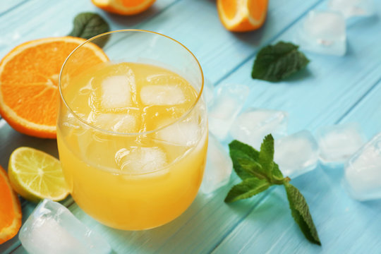 Glass with delicious orange juice, citrus fruits and mint leaves on wooden table