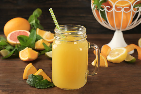 Glass jar with delicious orange juice and straw on wooden table