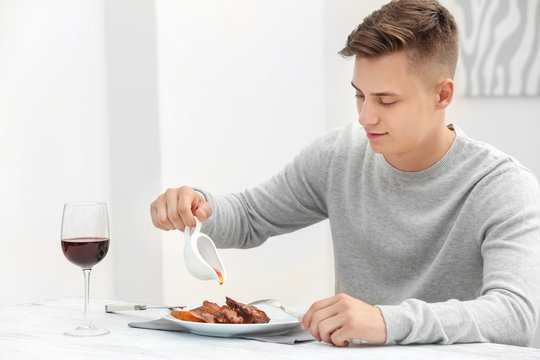 Young man eating delicious ribs in restaurant