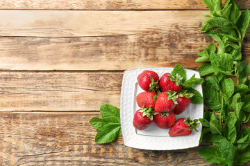 Plate with delicious strawberry and mint leaves on wooden table