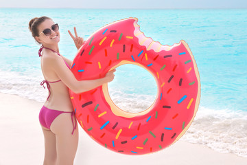 Beautiful young woman with colorful inflatable donut at sea coast
