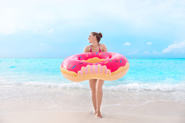 Naklejka na ściany i meble Beautiful young woman with colorful inflatable donut at sea coast