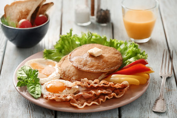 Tasty breakfast with fried eggs, pancakes, bacon and vegetables on table
