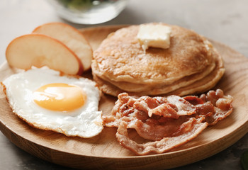 Tasty breakfast with fried egg, pancakes and bacon on wooden board