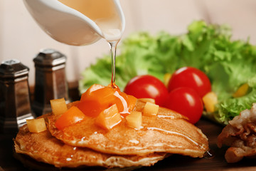 Pouring honey from gravy boat onto stack of delicious pancakes on wooden board