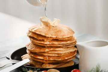 Pouring honey from gravy boat onto stack of delicious pancakes on plate
