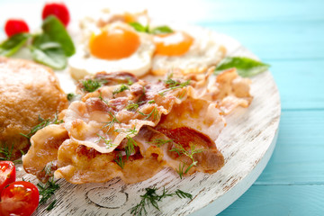 Tasty breakfast with fried eggs, pancakes and bacon on wooden board