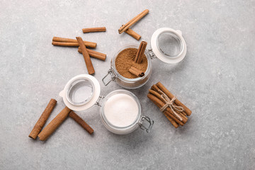 Composition with cinnamon and white sugar in glass jars on grey background