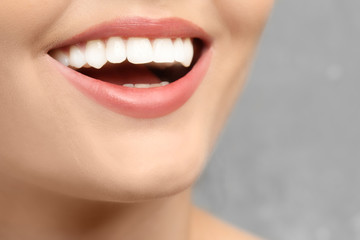 Young woman with healthy teeth laughing on grey background, closeup