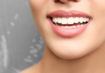 Young woman with healthy teeth laughing on grey background, closeup