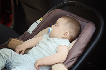 Adorable baby with pacifier sleeping in child safety seat inside of car