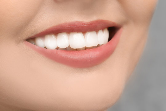 Young woman with healthy teeth on grey background, closeup