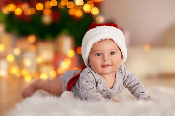 Cute little baby lying on floor against blurred Christmas lights