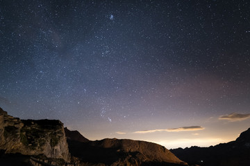 Obraz premium Night on the Alps under starry sky and the majestic rocky cliffs on the Italian Alps, with Orion constellation at the horizon.
