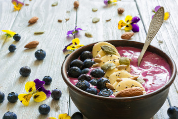 Smoothie bowl with chia seeds, blueberry, banana slices, nuts and flowers with a spoon