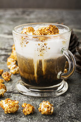 A glass of mouth-watering sweet milk coffee with a creamy foam topped with caramel crispy popcorn on a gray stone background. Selective focus.