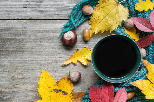 cup of coffee, scarf and autumn leaves on vintage wood background