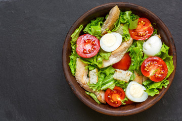 Caesar salad with croutons, quail eggs, cherry tomatoes and grilled chicken in a bowl