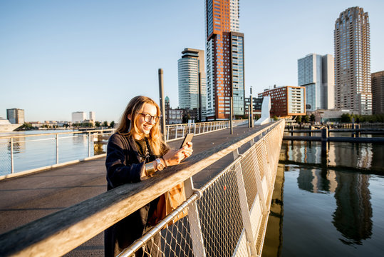 Woman standing with phone on the footbridge at the modern residential district during the morning in Rotterdam city